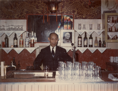 878016 Portret van Jih Peng Chen (1902), achter de bar in zijn Chinees restaurant Shanghai (Jacobskerkstraat 8) in Wijk ...